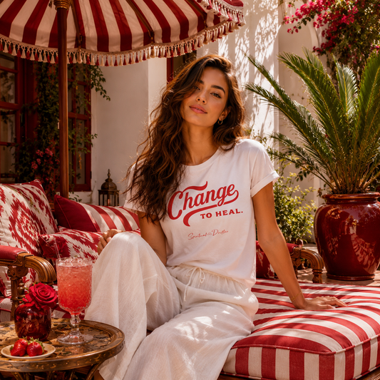 Woman sitting on a red and white striped chair under a striped umbrella with a drink and flowers on a table in a Moroccan Ryad. Spiritual lifestyle, positive vibes, aligned, positive mindset, conscious living & yoga clothing. Spiritual apparel inspired by modern mysticism, meditation, manifestation, sacred medicine and conscious living. Yoga and meditation clothing for awakened souls.The change to heal t shirt inspired by Dr Joe Dispenza. Healing through change