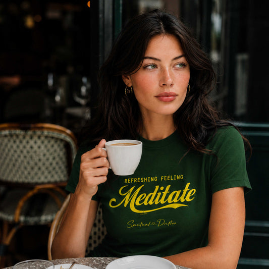 Woman holding a coffee cup with a green Spiritual Drifter t-shirt that says 'Meditate Refreshing Feeling Meditate" sitting in a café in Lake Como Italy.