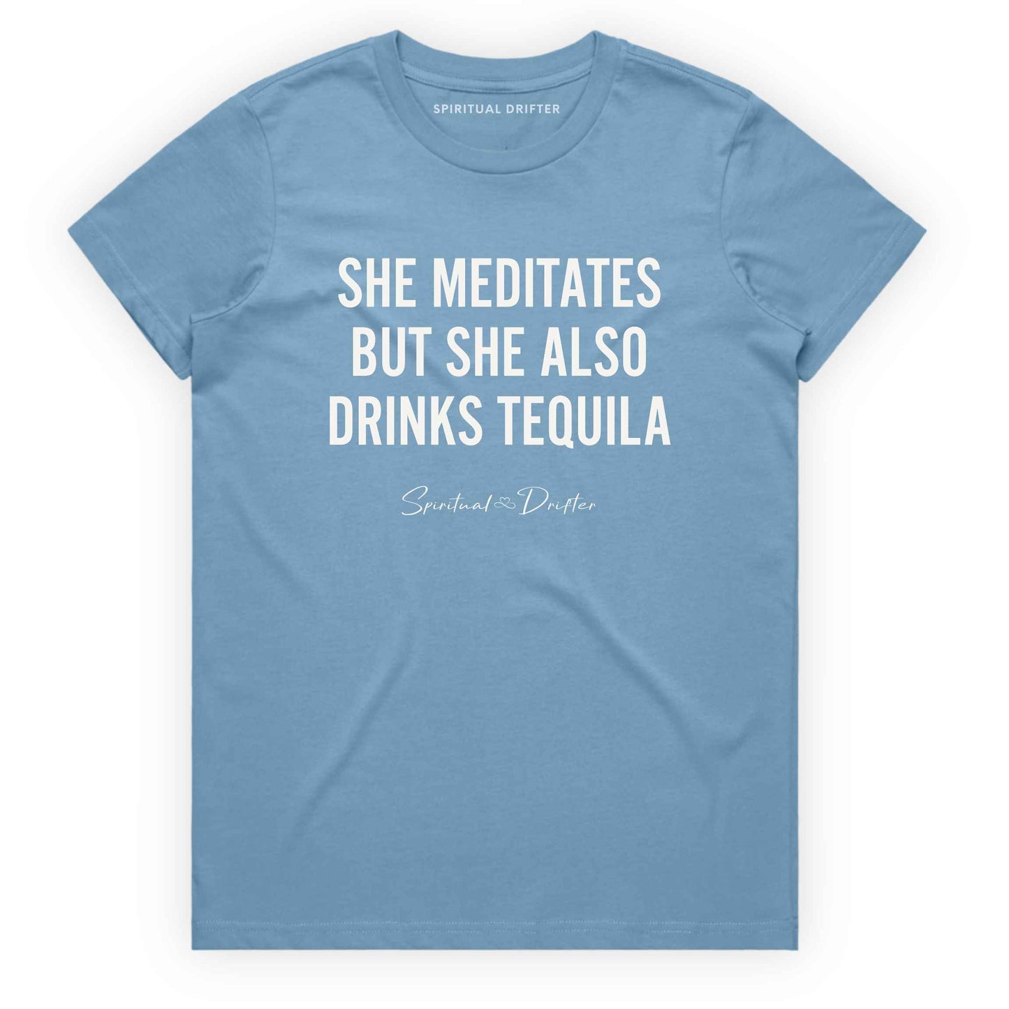Light Blue Spiritual Drifter t-shirt with white text 'SHE MEDITATES BUT SHE ALSO DRINKS TEQUILA' on a white background. Women's spiritual graphic tee. Relaxed beach lifestyle fashion for meditation lovers, yoga enthusiasts, wellness travelers, and free-spirited women. Meditation and yoga clothing for awakened souls.
