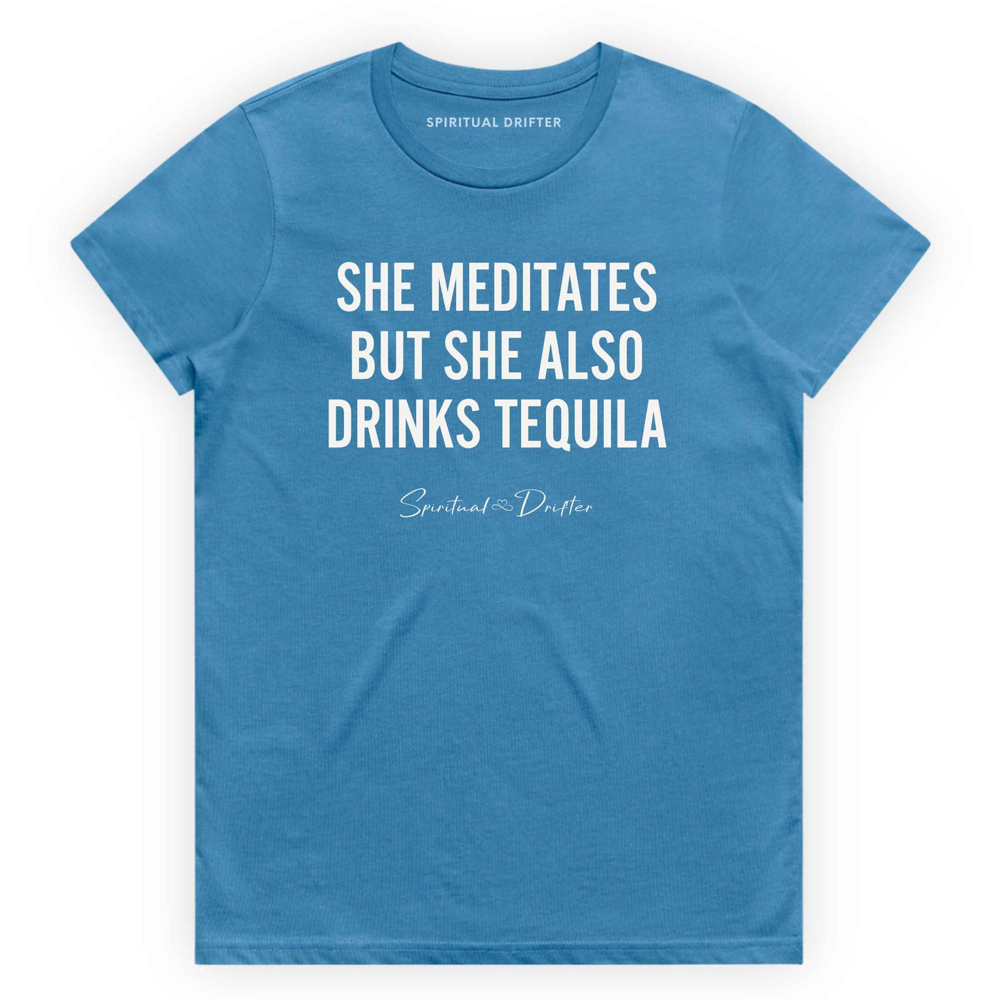 Hydro Blue Spiritual Drifter t-shirt with white text 'SHE MEDITATES BUT SHE ALSO DRINKS TEQUILA' on a white background. Women's spiritual graphic tee. Relaxed beach lifestyle fashion for meditation lovers, yoga enthusiasts, wellness travelers, and free-spirited women. Meditation and yoga clothing for awakened souls.
