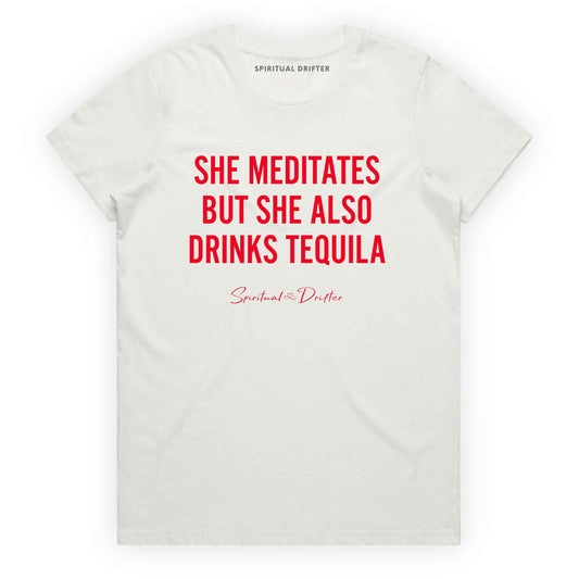 Natural Spiritual Drifter t-shirt with red text 'SHE MEDITATES BUT SHE ALSO DRINKS TEQUILA' on a white background. Women's spiritual graphic tee. Relaxed beach lifestyle fashion for meditation lovers, yoga enthusiasts, wellness travelers, and free-spirited women. Meditation and yoga clothing for awakened souls.