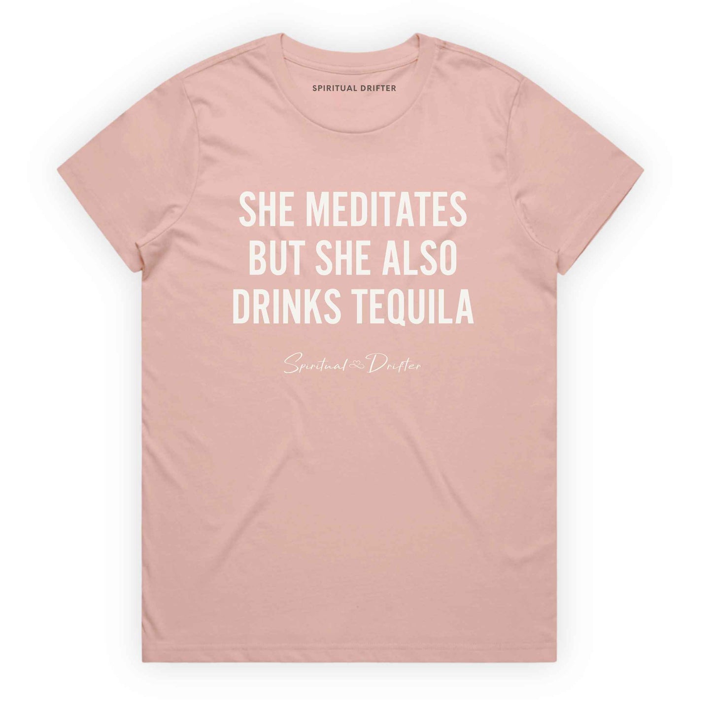 Soft Pink Spiritual Drifter t-shirt with white text 'SHE MEDITATES BUT SHE ALSO DRINKS TEQUILA' on a white background. Women's spiritual graphic tee. Relaxed beach lifestyle fashion for meditation lovers, yoga enthusiasts, wellness travelers, and free-spirited women. Meditation and yoga clothing for awakened souls.