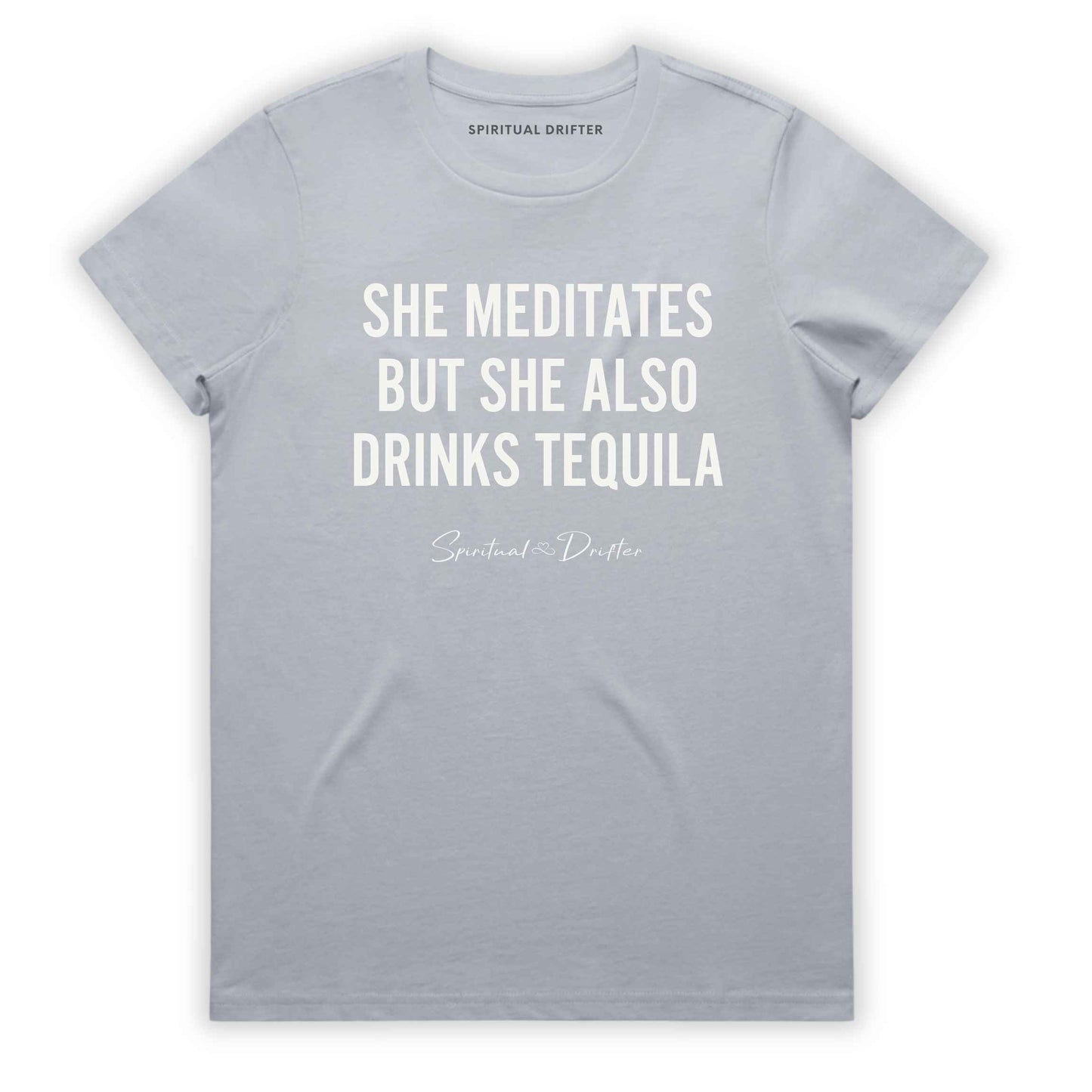 Powder light gray Soft Pink Spiritual Drifter t-shirt with white text 'SHE MEDITATES BUT SHE ALSO DRINKS TEQUILA' on a white background. Women's spiritual graphic tee. Relaxed beach lifestyle fashion for meditation lovers, yoga enthusiasts, wellness travelers, and free-spirited women. Meditation and yoga clothing for awakened souls.