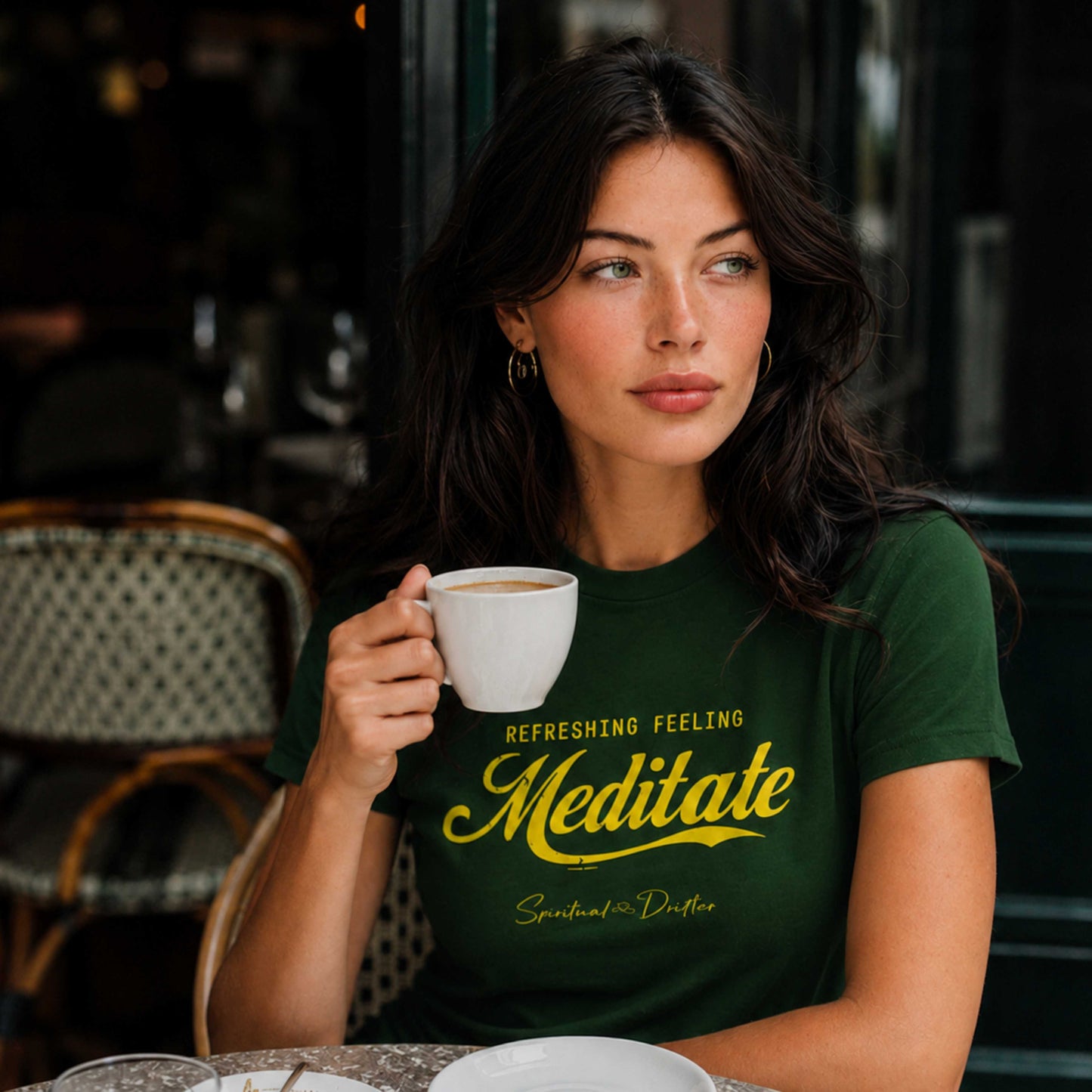Woman holding a coffee cup with a green Spiritual Drifter t-shirt that says 'Meditate Refreshing Feeling Meditate" sitting in a café in Lake Como Italy.