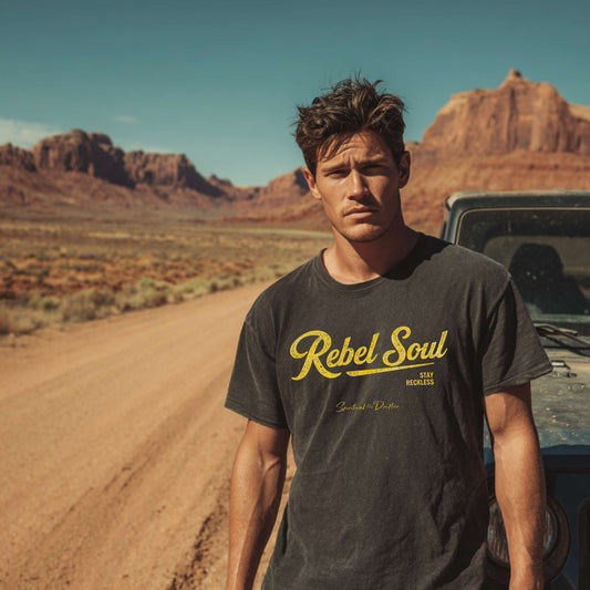 Man wearing a 'Rebel Soul' t-shirt in a desert setting with mountains in the background. Spiritual lifestyle, positive vibes, aligned, positive mindset, conscious living clothing.