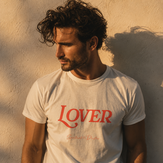 Man wearing a white t-shirt with 'LOVER' printed on it against a neutral wall background. Spiritual Drifter “Lover” graphic unisex organic cotton t-shirt in white – elevated spiritual apparel inspired by mindfulness, manifestation, coherence, meditation, and living in a state of surrender and love.