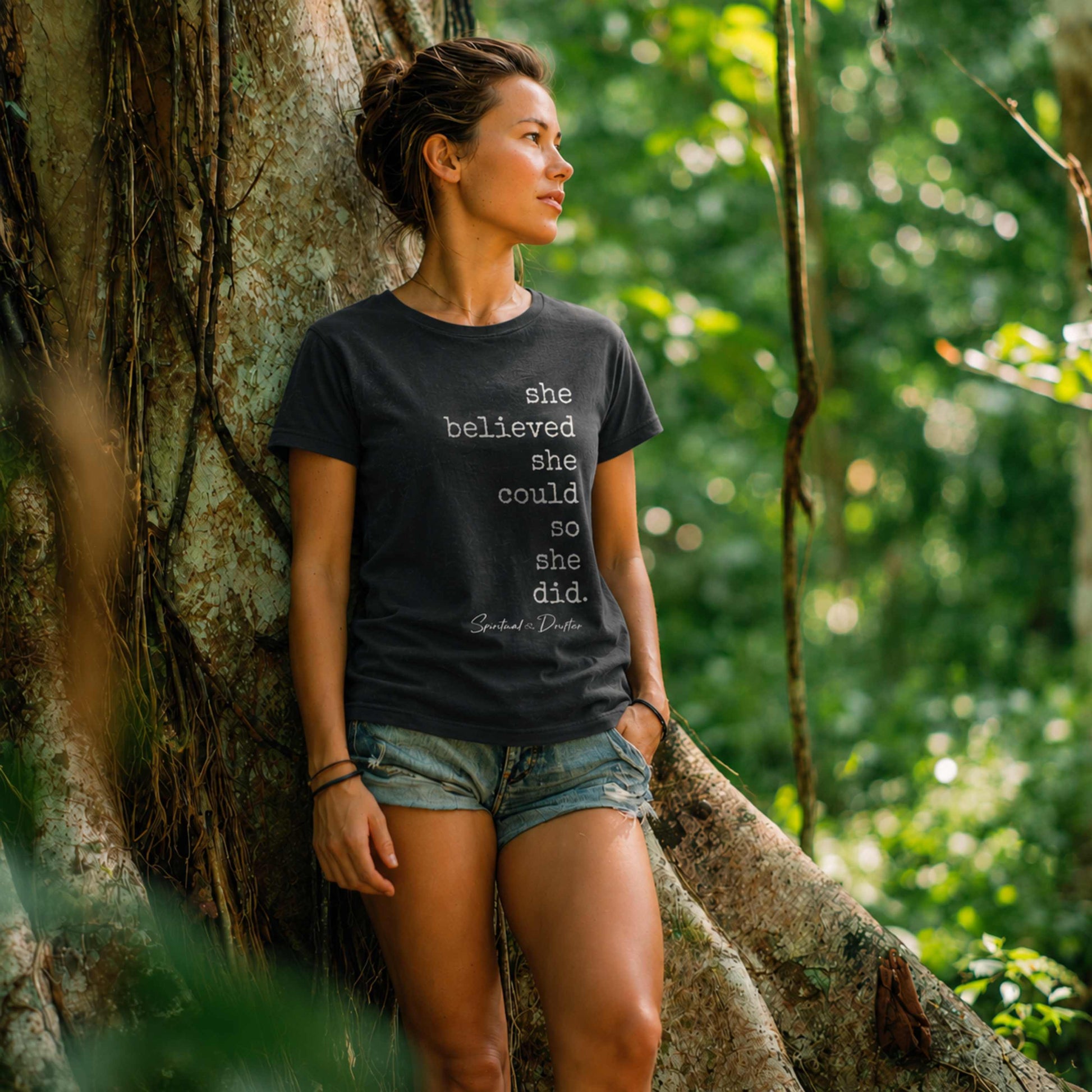 Woman in Amazon jungle standing next to a tree wearing Spiritual Drifter charcoal shirt with graphic "She believed she could so she did" inspirational conscious cotton clothing. Inspired by Sacred medicine, yoga, meditation retreat life.