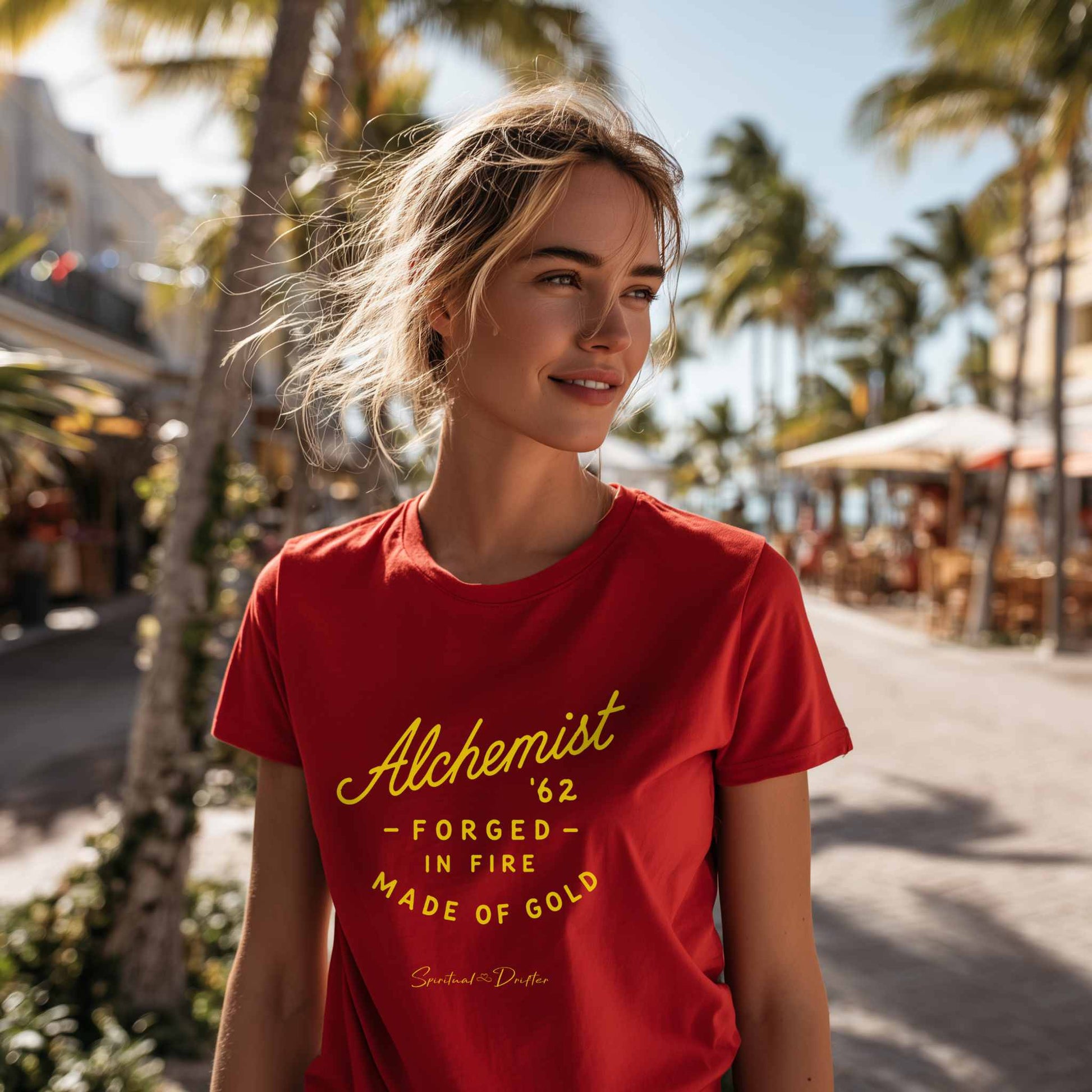 Woman wearing a red t-shirt with yellow graphic "Alchemist forged in fire" in a tropical setting. Spiritual Drifter  – elevated spiritual apparel inspired by mindfulness, manifestation, coherence, meditation, and living in a state of initiation.
