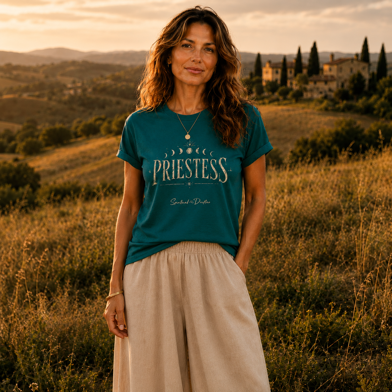 Model wearing the Spiritual Drifter “Priestess Lunar Cycle” graphic classic t shirt in teal, standing in a field in Tuscany, Italy. Elevated spiritual apparel inspired by meditation, mindfulness, yoga, positive vibes, law of attraction and conscious living. Become the Priestess in this elevated natural fashion tee for women.